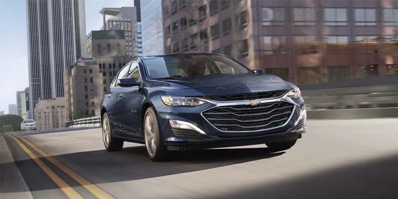 Dark-colored Chevrolet Malibu sedan driving through a downtown area