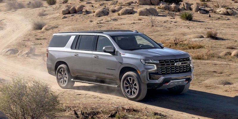 Silver full-size SUV driving on a dusty desert trail, with smaller views showing the vehicle from the rear on an off-road path