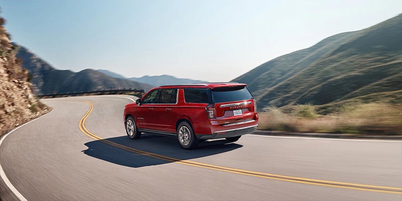 White full-size SUV driving along a curving mountain road bordered by rocky hillsides.
