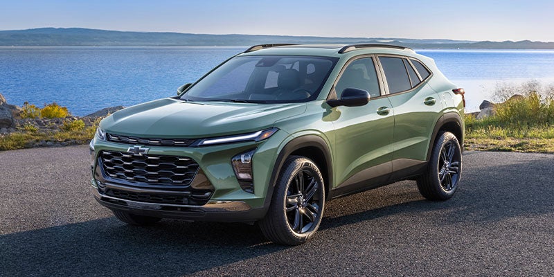 Light green Chevrolet SUV parked on a coastal roadway with a large body of water visible in the background.