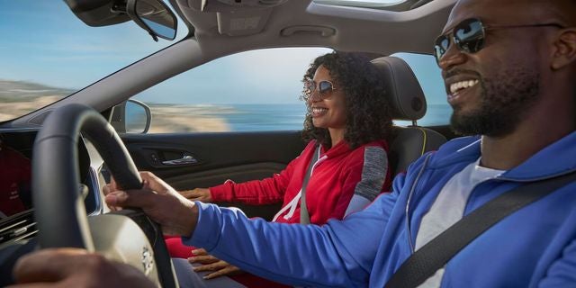 Two occupants seated inside a Chevrolet SUV cabin during a drive with the road and landscape visible through the windows.